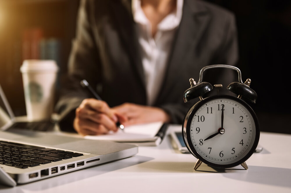 Source Adobe stock free. Picture of woman in business suit sittin gat table with alarm clock in foreground.