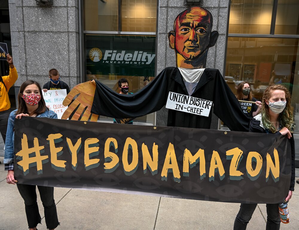 Photo by Joe Piette. Amazon workers holding banner which reads hashtag eyes on amazon