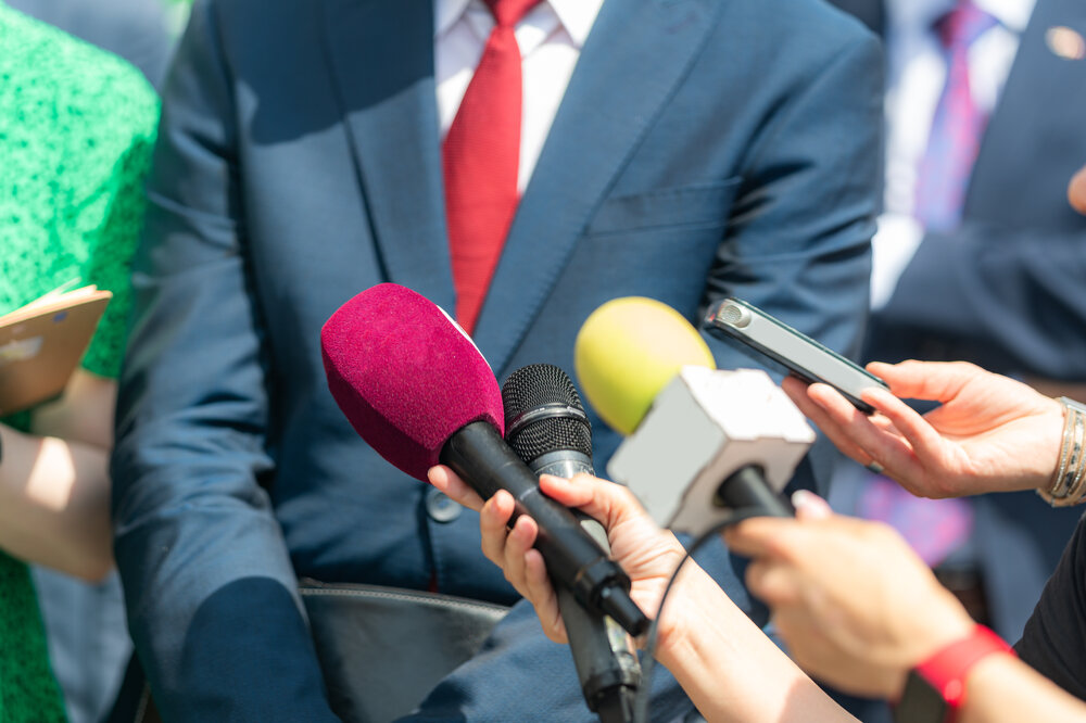Source: Adobe free. Photograph of several microphones being thrust toward man in suit